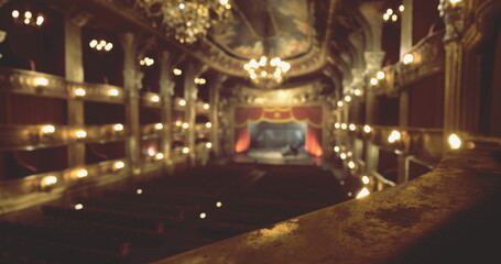 Inside a beautifully designed theater, warm lights illuminate ornate decorations as the stage awaits a performance. Rows of seats create an inviting atmosphere for attendees.