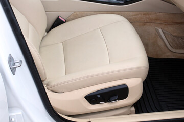 Close-up of beige leather car seat with power adjustment controls, black floor mat, and detailed stitching, showcasing comfort and premium interior design. Beige leather car interior in lux car.