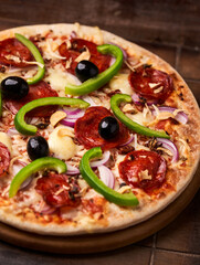 Pizza with chorizo ​​sausage, mozzarella cheese, green pepper and black olives. Rustic wooden background. Soft focus.	