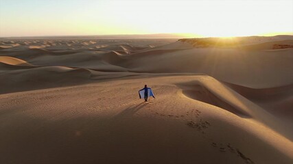Lonely woman in a blue robe walking along a sand dune crest during a scenic desert sunset in Morocco - Powered by Adobe