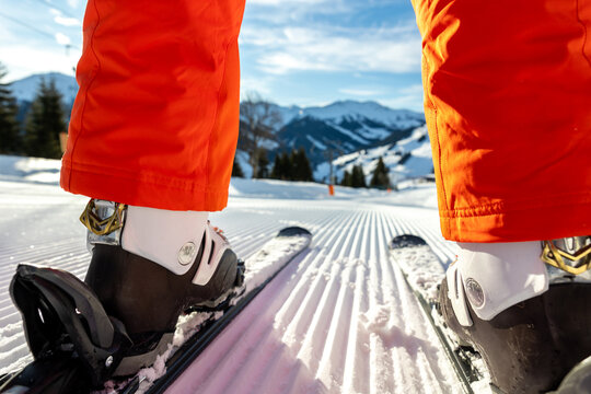 Scenic back POV view beginner skier close-up legs downhill start line rows freshly prepared groomed ski slope piste bright warm morning sunrise sky background. mountain landscape winter resort