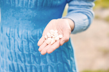 Close-up of a woman's hand with white pills in a blue sweater, symbolizing vitamins, supplements, medication and health care outdoors