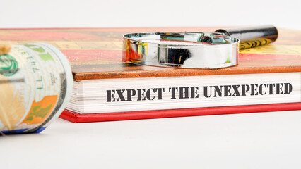 Expect The Unexpected word on the end of the book on a white background and compositions with a magnifying glass and money