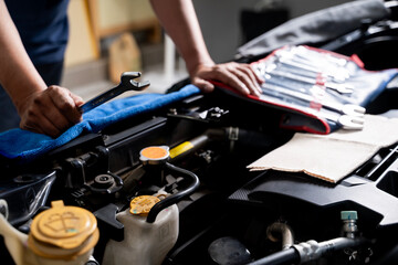 Young man fixing car engine by himself at home, concept of DIY repair, maintenance, and saving money on vehicle service.