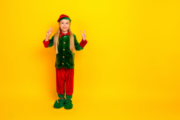 Joyful young girl dressed in a traditional Christmas elf costume poses cheerfully against a vibrant yellow background, spreading holiday cheer.