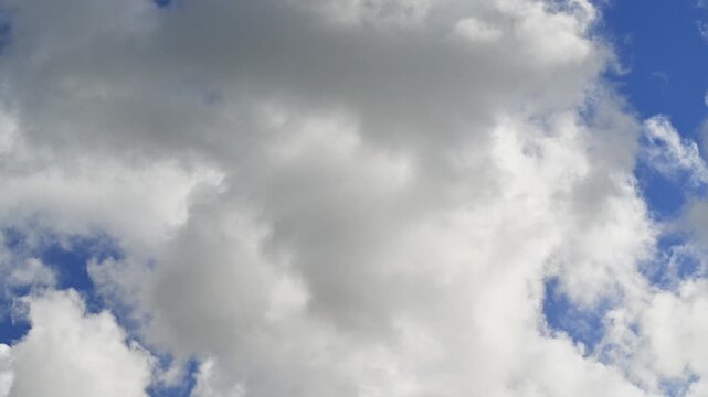 White fluffy clouds crossing the blue sky from left to right in timelapse. Fair-weather cumulus clouds. Dreamlike skyscape.