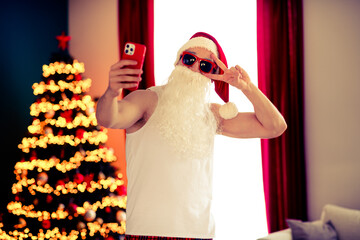 Festive Santa Claus in Sunglass Taking a Selfie Near a Decorated Christmas Tree in a Cozy Home...