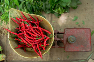 Red chilies on a vintage scale, artfully surrounded by fresh green vegetables, showcasing market freshness