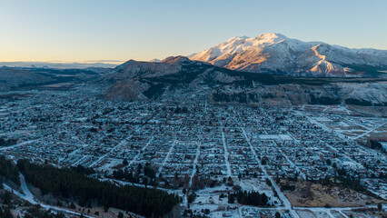 Winter aerial view of Esquel city at sunrise, covered in snow, with the Andes mountains in the...