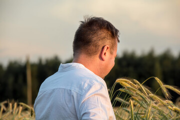 Man standing in a field of rye at sunset, viewed from behind, wearing a white shirt, peaceful scene in nature with warm evening light.