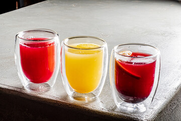 Three colorful drinks sit in glass cups on a smooth surface, inviting a refreshing experience