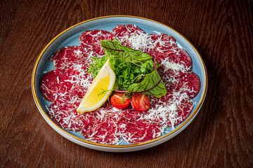 A beautifully arranged plate of beef carpaccio garnished with greens, tomatoes, and lemon slices