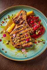 Juicy pork chop on a colorful plate, accompanied by sweet corn and a fresh salad of peppers