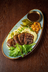 Grilled meat with soft mashed potatoes, fresh greens, and pickles makes a perfect dish