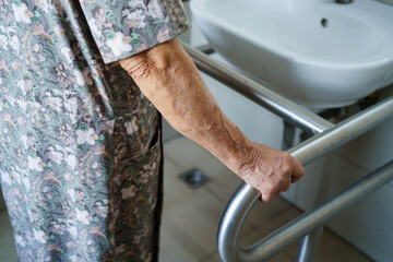 Asian elderly woman patient use toilet support rail in bathroom.