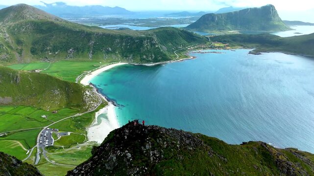 Breathtaking aerial perspective showcasing Mannen peak overlooking Haukland beach in Lofoten, Norway. This scenic spot features lush green landscapes and turquoise waters under a clear blue sky.