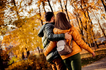 Romantic couple walking together through an autumn park on a sunny day, surrounded by vibrant fall foliage.