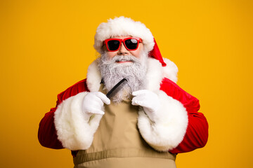 Funky Santa Claus with red sunglasses combing beard against bright yellow background showcasing festive holiday spirit