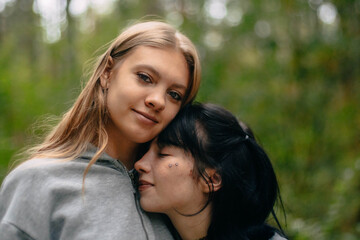 Obraz premium Two young women share a tender moment in a lush green forest. One rests her head on the other's shoulder while both smile lightly, enjoying their friendship in nature.