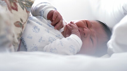 Newborn baby lying in bed, gesticulating with hands and making slight grimaces. baby surrounded by...