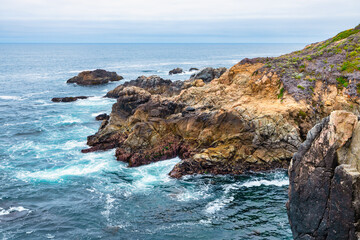 Dramatic Big Sur coastline along Highway 1, California. Waves crash against rugged cliffs, forming turquoise patterns in the Pacific Ocean, showcasing the raw beauty of the California coast