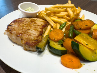 Grilled pork chop with french fries and sautéed vegetables on white plate