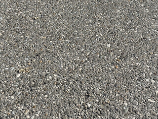 Textured asphalt surface with pebbles and small stones in sunlight