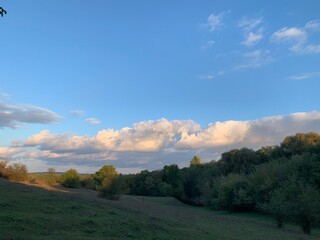 Scenic landscape with green meadow, trees, and dramatic clouds in the blue sky at sunset. Peaceful nature background.
