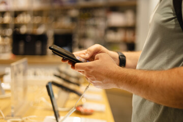 Closeup of man testing smartphone at electronics store showcase.