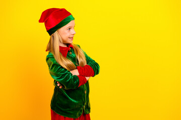 Young girl dressed as a Christmas elf in a colorful costume standing confidently against a vibrant yellow background