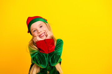 Adorable young girl dressed as a Christmas elf posing cheerfully against a festive yellow background, spreading holiday joy
