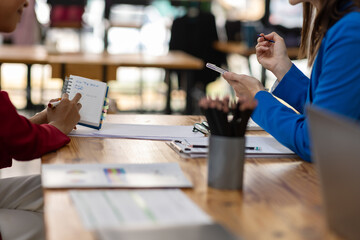 Businesswoman having meeting taking notes using smartphone in modern office. Two businesswomen in a bright office, discussing plans and taking notes on a smartphone.