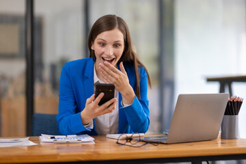 Businesswoman smiling and using smartphone in modern office. Businesswoman is working in office, using a smartphone and smiling.