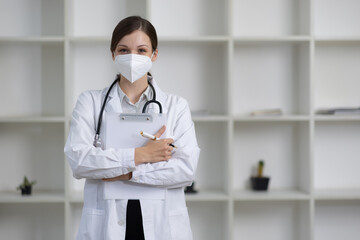 Confident female doctor in a modern clinic, holding a clipboard and wearing a protective mask, conveys reassurance and dedication, providing professional care in a bright and clean office setting.