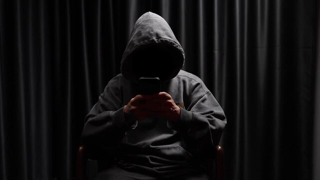 Anonymous hooded hacker texting on smartphone
