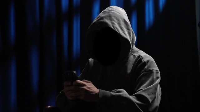 Anonymous hooded hacker using a smartphone