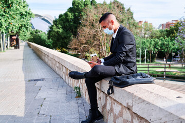 Obraz premium Businessman in suit checking phone at park with coffee during sunny day