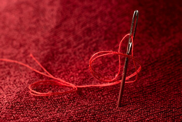 A needle and thread on red fabric. Sewing supplies
