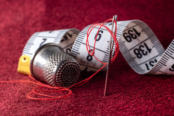 A needle and thread, a tape measure, and a thimble are lying on the fabric. Sewing supplies