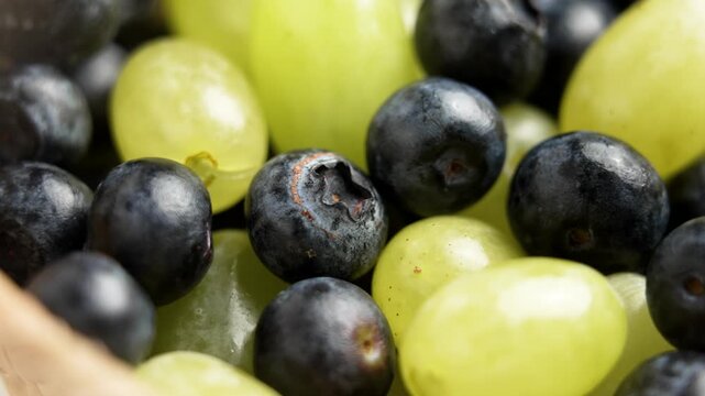 A berry assortment of fresh blueberries and green grapes in paper grocery packaging. Rotation