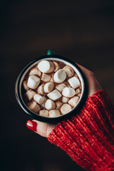 Cup of cocoa or hot chocolate with marshmallows in female hand, top view.