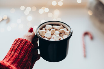 Woman hand holding a cup of hot chocolate with marshmallows at home.