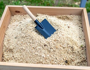 Wooden box filled with light beige sand, a small black shovel inside