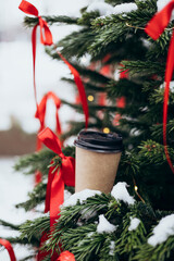 A cup of coffee on the branches of a Christmas tree decorated with red bows.