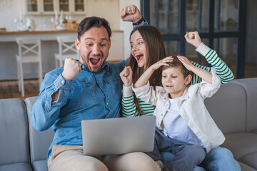 Glad Caucasian family with laptop, credit card make victory, success gesture with hand in living room interior. Win, ad and offer at home, reaction to good news, sale and cashback