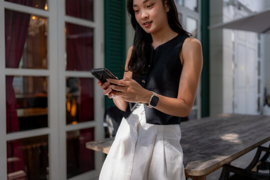 Asian woman using smartphone, smartwatch at outdoor cafe