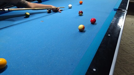 Pool Table Action: Player Aims Cue Across Blue Felt Toward The Scattered Balls