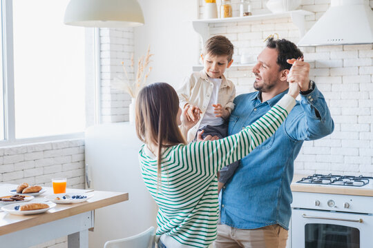 Photo of a happy family of three having fun and dancing with a child boy at kitchen at home. Portrait of young parents spending time together with son. Care and love parenting concept.