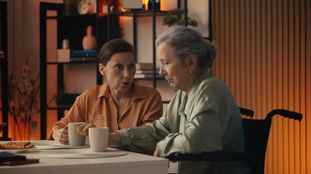 Senior woman sharing gossip with female friend in wheelchair, warm companionship