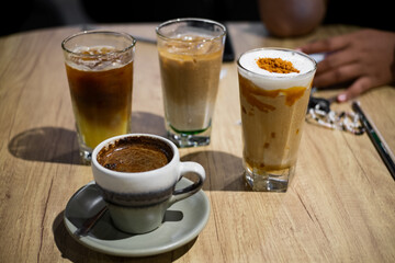 A variety of hot and cold coffee drinks including cappuccino , black, and iced coffee on a wooden table at the cafeteria.
